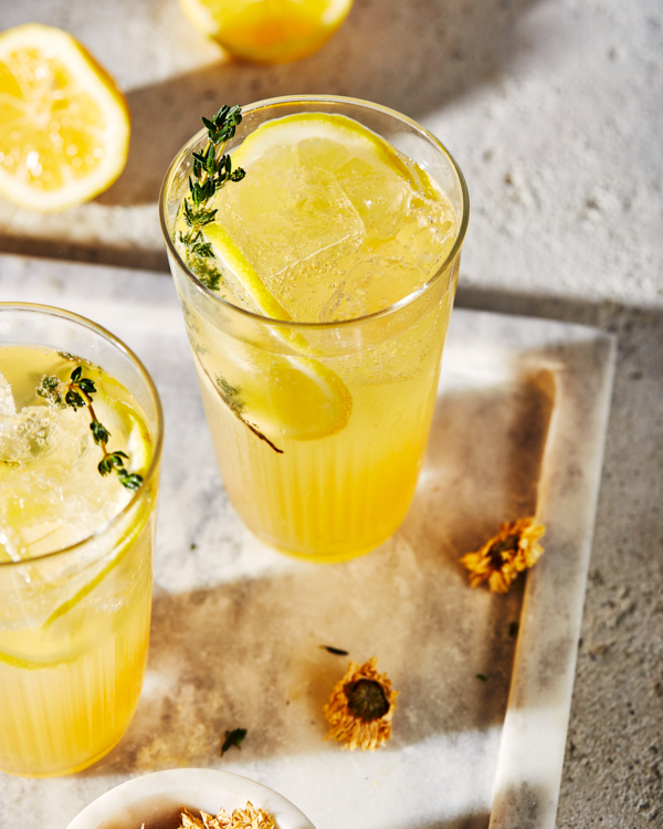 Deux verres de limonade pétillante au thé au chrysanthème sur un plateau en marbre, servis avec des tranches de citron et des brins et fleurs de chrysanthème