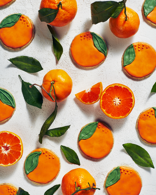 Biscuits sablés décorés en forme d'orange avec des oranges entières, des oranges en tranches et des feuilles d'oranger.