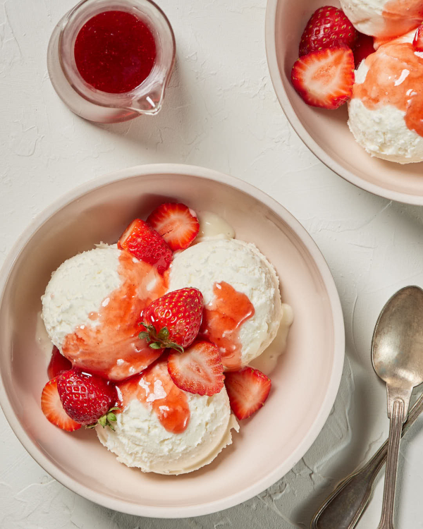 Deux bols rose pâle de crème glacée à la vanille garnis de fraises tranchées et de sauce aux fraises.