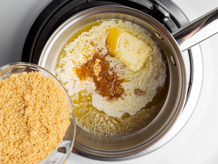 Cassonade dorée versée dans une casserole contenant un mélange frémissant de sucre, de beurre et de miel