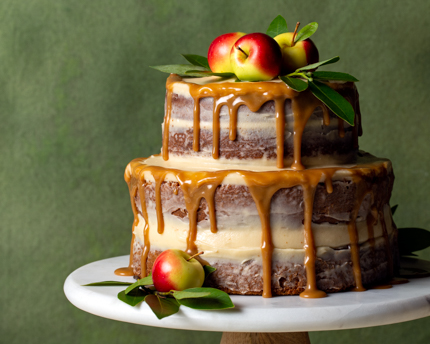 Sur fond vert, gâteau nu pommes et épices sur un présentoir à gâteau déposé sur une table, avec des pommes
