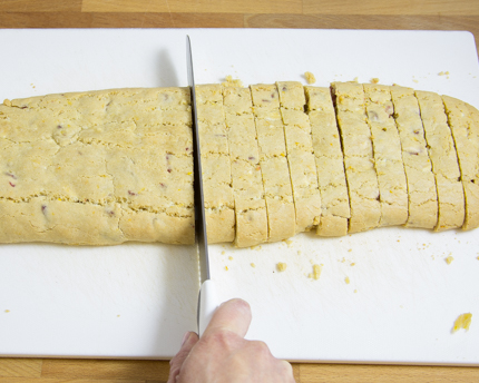 Le découpage d’un rouleau de biscotti doré sur une planche à découper avec un couteau dentelé