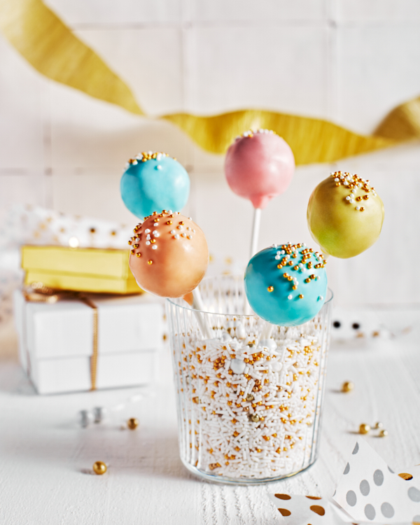 Cake pops de couleur pastel avec des éclats de verre dans un verre d'éclats de verre, présentées avec des décorations de fête et des cadeaux blancs et or.
