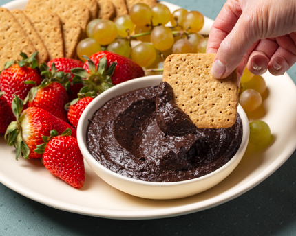 Bol de houmous au chocolat sur un plateau avec des biscuits Graham, des figues, des fraises et des raisins
