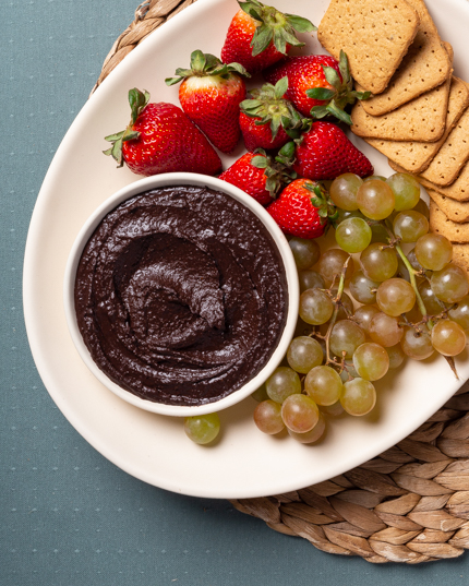 Bol de houmous au chocolat sur un plateau avec des biscuits Graham, des fraises et des raisins