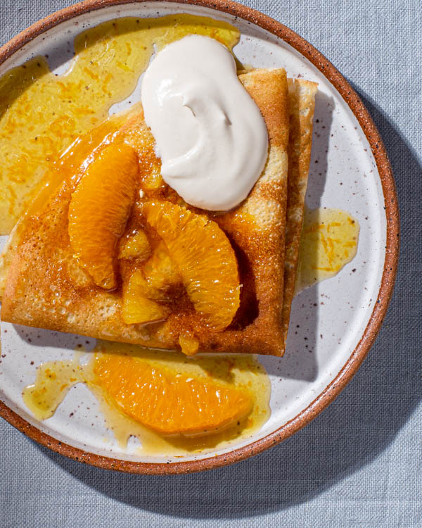 Une crêpe sur une assiette garnie de beurre Suzette, de quartiers d'orange et de crème sure fouettée à la cassonade