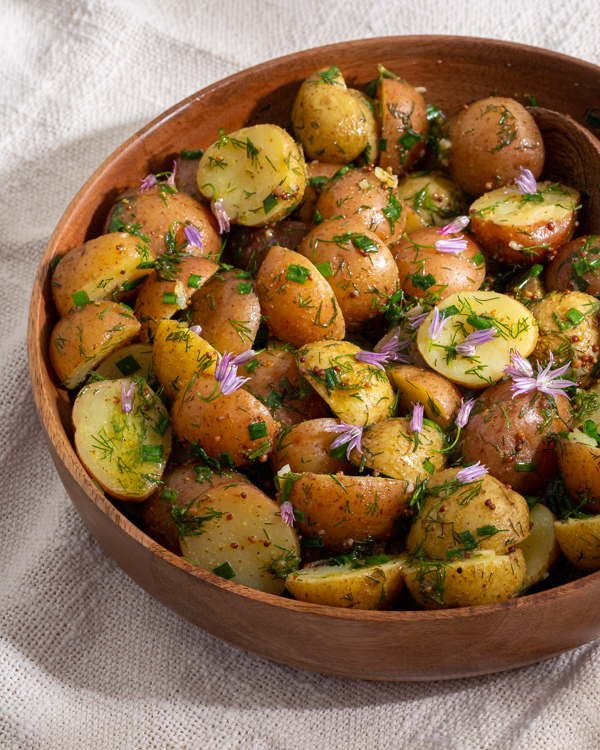 Salade de pommes de terre à l’aneth décorée de pétales de fleurs et d’oignons verts dans un bol en bois sur une nappe
