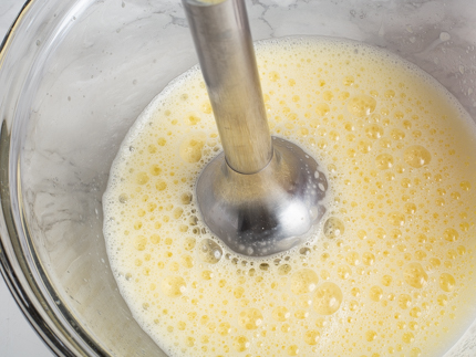 Œufs et lait mélangés dans un bol en verre avec un mélangeur à immersion