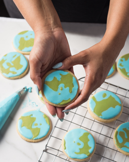 Des mains qui, à partir d'une grille de refroidissement, soulèvent un biscuit au beurre décoré de glaçage bleu et vert