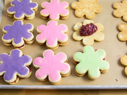 Biscuits en forme de fleurs sur une plaque à pâtisserie, décorés de glaçage coloré et fourrés de garniture aux framboises