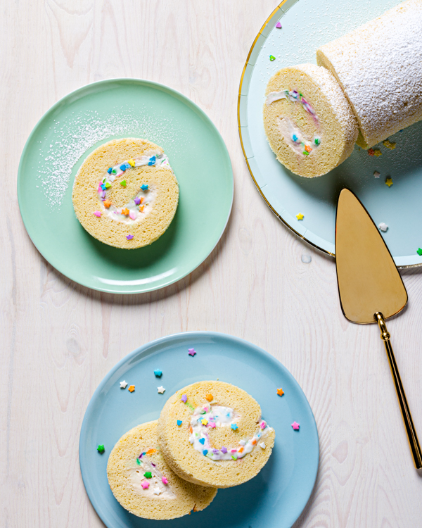 Roulé de gâteau blanc sur une assiette, quatre tranches coupées sur des assiettes de couleurs pastel avec une pelle à gâteau or