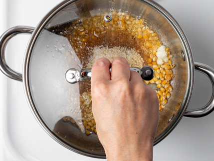 Une casserole avec son couvercle, du sucre fondant et des grains de maïs qui éclatent