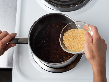 Verser le sucre turbinado à partir d’un bol en verre dans une casserole avec de l’eau chaude et des feuilles de thé