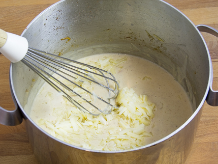 Casserole avec du lait et du fromage râpé se faisant incorporer à l’aide d’un fouet
