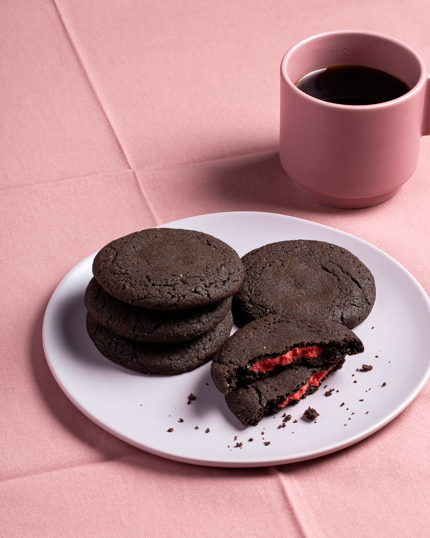 Une assiette de biscuits au chocolat noir farcis de pâte d’amande rouge, avec une tasse de café