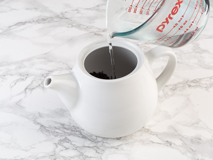  Eau bouillante qui se fait verser d’une tasse à mesurer dans une théière contenant des feuilles de thé et la liqueur