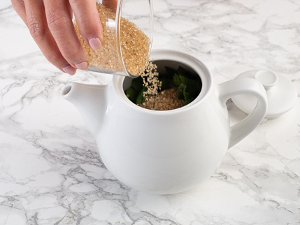 Sucre turbinado qui se fait verser d’une tasse à mesurer dans une théière remplie de thé à la menthe