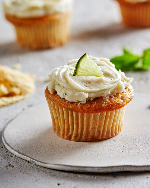 Un cupcake mojito avec un glaçage d'hermine sur une assiette, garni d'un quartier de citron vert.