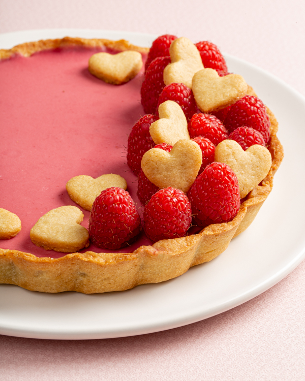 Tarte panna cotta framboises et eau de rose décorée de framboises et de biscuits en forme de cœur avec deux fourchettes
