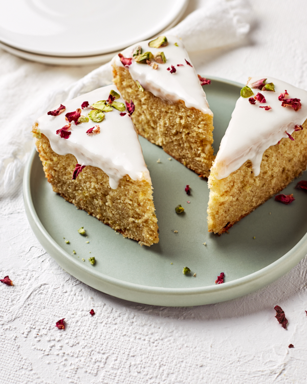 Trois parts de gâteau d’amour persan glacé décorées de pétales de roses et disposées sur une assiette vert pâle.