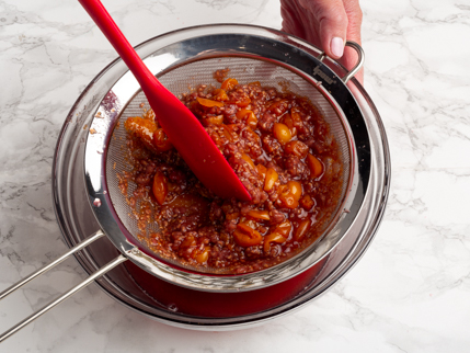 Égoutter les framboises et les groseilles cuites à l’aide d’une passoire et d’une spatule au-dessus d’un bol en verre
