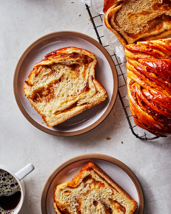 Tranches de babka aux pommes épicées dans des assiettes, avec le pain coupé sur une grille de refroidissement et une tasse de café.