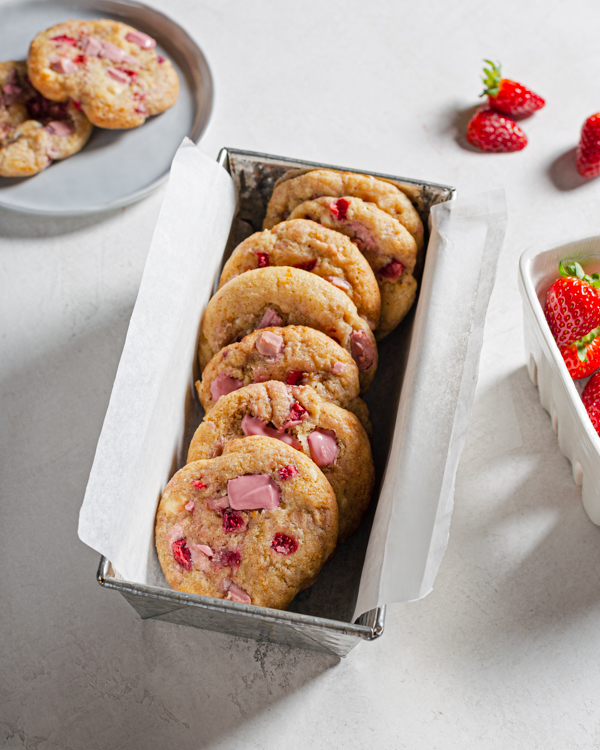 Une boîte de conserve recouverte de papier parchement et remplie de cookies aux fraises et au chocolat rubis.