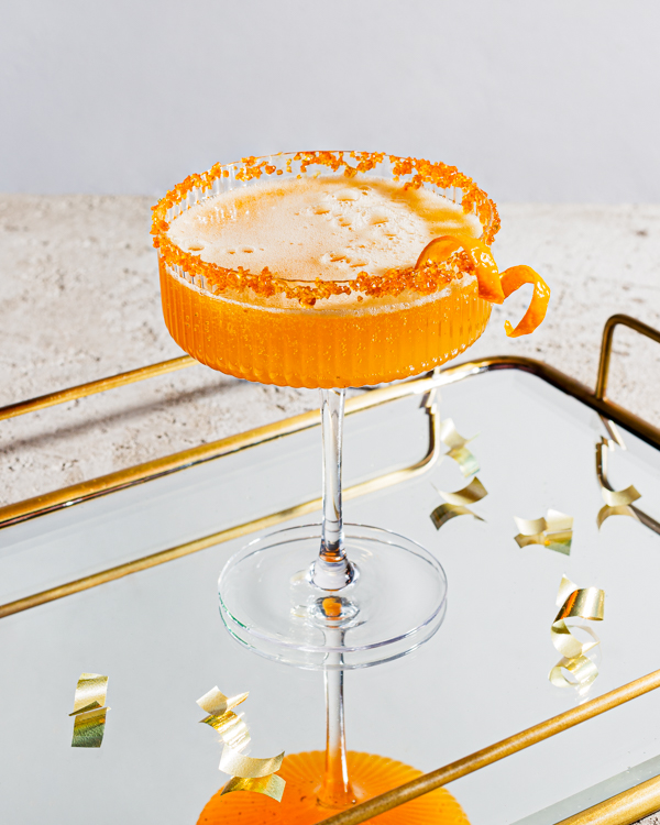 Un verre de cocktail pétillant au gingembre et au curcuma garni d'écorces d'orange et bordé de sucre