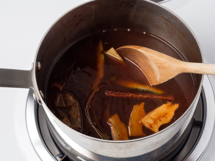 Du jus de fruit et des assaisonnements se faisant remuer dans une casserole à l’aide d’une cuillère de bois