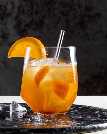 Un verre de cocktail au whisky, à l’orange et au gingembre bien frais avec des glaçons, sur un plateau en marbre