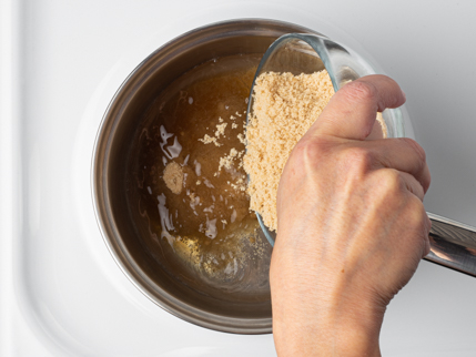 Verser la cassonade dorée d’un bol en verre dans une casserole remplie d’eau sur une cuisinière