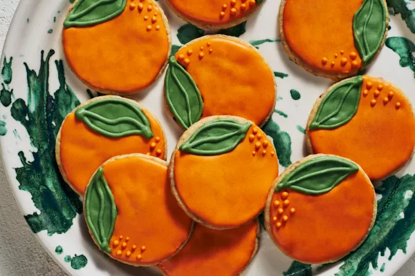 Des biscuits sablés décorés en forme d'oranges sur une assiette blanche et verte.