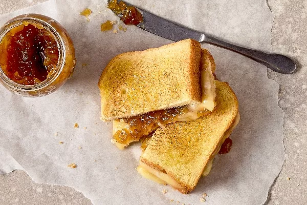 Vue aérienne d’un sandwich au fromage grillé à la confiture d’oignons coupé en deux, déposé sur du papier parchemin. Le sandwich est doré et révèle du fromage fondu et de la confiture d’oignons caramélisés