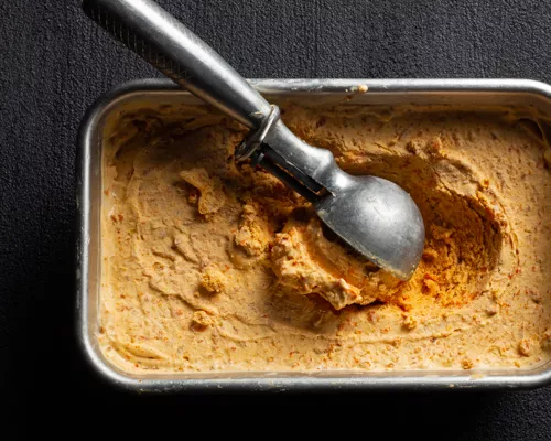 Crème glacée aux carottes dans un récipient en métal avec une cuillère à crème glacée