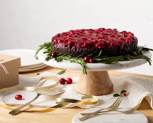 Gâteau au chocolat renversé aux canneberges présenté sur une assiette sur pied décorée de romarin et de canneberges