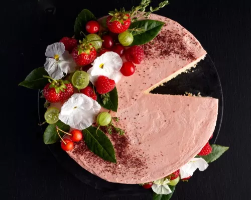 Gâteau avec meringue suisse crème au beurre rose, disposé sur une assiette à gâteau et décoré de fleurs, de verdure et de petits