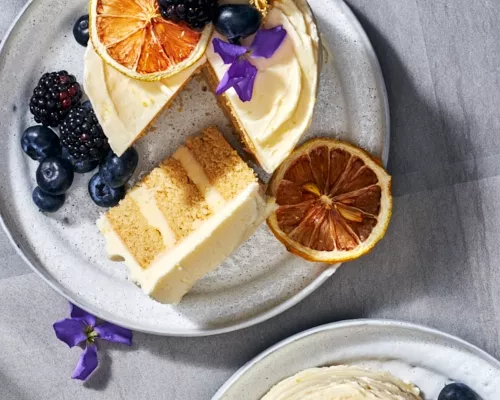 Un mini-gâteau au citron et à la camomille sur une assiette avec une tranche coupée, servi avec des baies et garni de baies