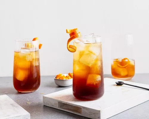 Trois verres de spritz café infusé à froid et orange avec glaçons et garnis de zeste d’orange en bandelettes.