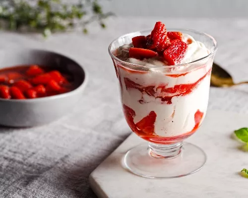Fool aux fraises dans un verre à parfait sur une plaque marbrée avec un bol de sauce aux fraises