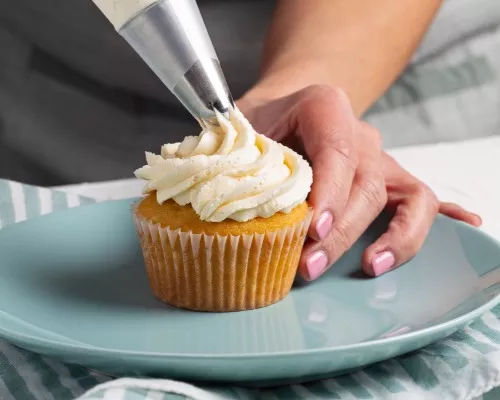  Une femme glaçant un cupcake à la vanille à l’aide d’une poche à pâtisserie avec une pointe en métal