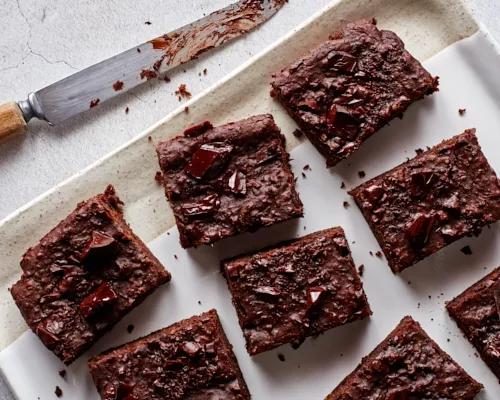 Des brownies végétaliens garnis de morceaux de chocolat noir sur un plateau avec un couteau.