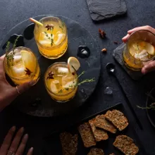 Mains approchant des verres de cocktail à la pomme et aux épices pour tarte à la citrouille servies avec des craquelins
