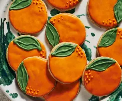 Des biscuits sablés décorés en forme d'oranges sur une assiette blanche et verte.