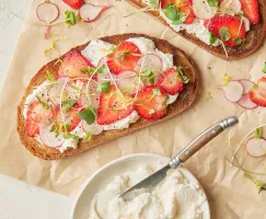 Deux tranches de pain grillé garnies de ricotta fouettée à la cassonade, de fraises et de radis tranchés, ainsi que de micro-pousses.