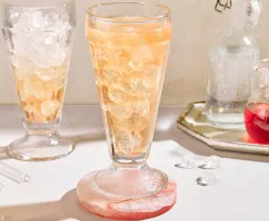 Deux verres de julep à la menthe sans alcool avec de la glace pilée et garnis de menthe, servis sur un plateau blanc et présentés avec un bol de feuilles de menthe, une moitié de lime, une carafe de julep préparé et une carafe de sirop simple à la menthe.