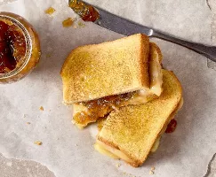 Vue aérienne d’un sandwich au fromage grillé à la confiture d’oignons coupé en deux, déposé sur du papier parchemin. Le sandwich est doré et révèle du fromage fondu et de la confiture d’oignons caramélisés