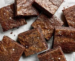 Brownies carrés garnis de sel en flocons reposant sur du papier parchemin.