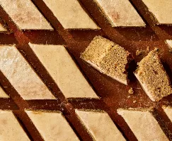Des rangées de barres de gâteau épicées coupées en losanges et surmontées d'un glaçage lisse. Une barre est cassée en deux, révélant un intérieur moelleux et friable. Le fond brun chaud semble rustique et confortable.