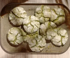Une fournée de biscuits craquelés au matcha fraîchement sortis du four qui refroidissent sur une plaque à biscuits, montrant leurs surfaces craquelées et leur enrobage de sucre en poudre.