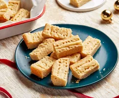 Des sablés sur une assiette bleue avec des rubans rouges et des ornements dorés de Noël